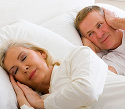 Man covering his ears while a woman sleeps peacefully